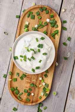 Bowl of tasty sour cream with green onion on light wooden background clipart