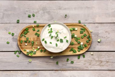 Hafif ahşap arka planda yeşil soğanlı bir kase lezzetli ekşi krema