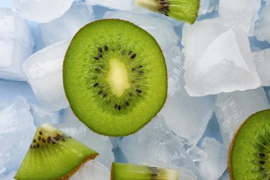 Mavi arka planda dilimlenmiş taze kivi ve buz.