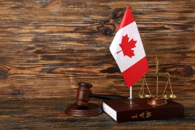 Kanada bayrağı, yargıç tokmağı, adalet terazileri ve ahşap zemin üzerine hukuk kitabı.