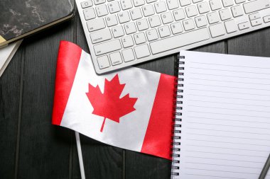 Koyu ahşap arka planda dizüstü bilgisayar ve bilgisayar klavyeli Kanada bayrağı, yakın plan