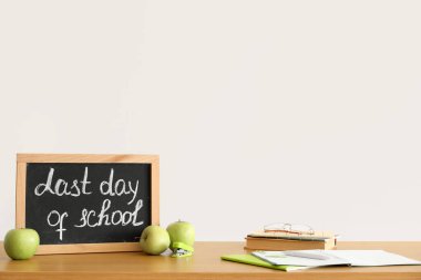 Okulun son günü yazılı tebeşir tahtası, ışık duvarının yanındaki masada elmalar ve defterler