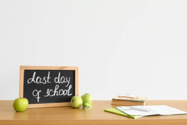 Okulun son günü yazılı tebeşir tahtası, ışık duvarının yanındaki masada elmalar ve defterler