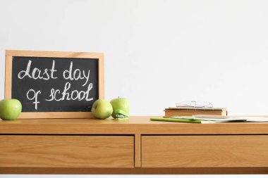 Okulun son günü yazılı tebeşir tahtası, ışık duvarının yanındaki masada elmalar ve defterler