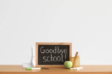 Işık duvarının yanındaki masa üzerinde GOODBYE OKULU, elma ve kırtasiye yazı tahtası