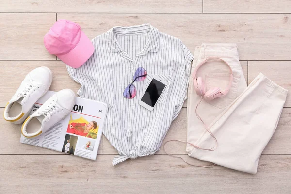 Stylish clothes with accessories, headphones, mobile phone and newspaper on light wooden floor