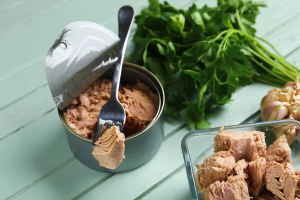 stock image Opened tin can and bowl with delicious tuna on green wooden table, closeup