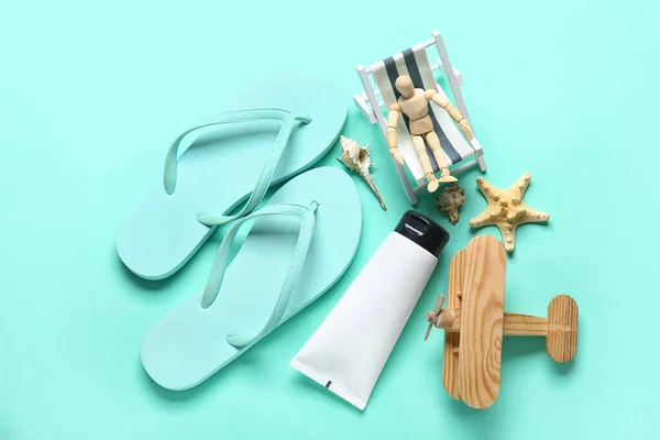 Composition with beach accessories and wooden mannequin sitting in miniature deck chair on turquoise background
