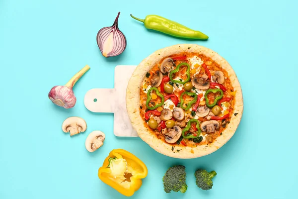 Board with vegetable pizza and ingredients on blue background