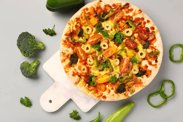 Board with vegetable pizza on grey background