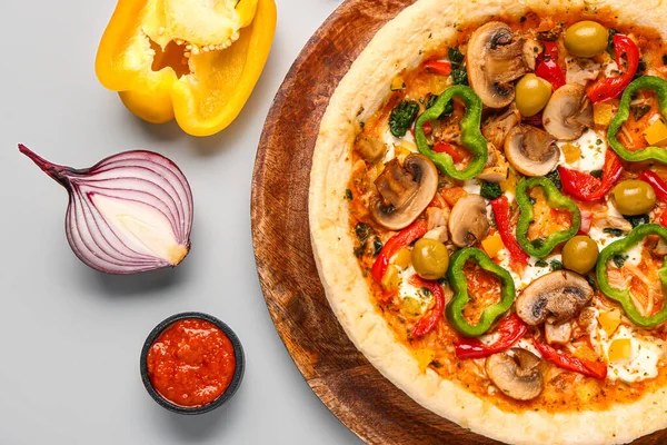 Board with vegetable pizza and ingredients on grey background