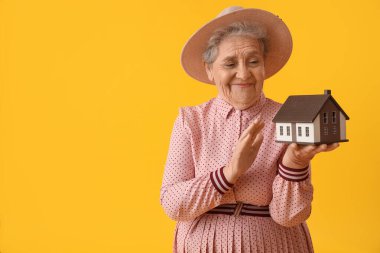 Senior woman with house model on yellow background clipart