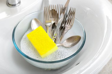 Çatal bıçak takımı ve temizleme süngeri lavaboda, yakın plan.