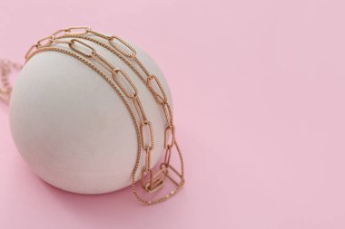 Pembe arka planda altın kolyeli heykel