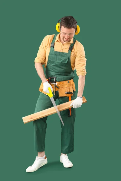 男性木匠在绿色背景上锯木木板 — 图库照片