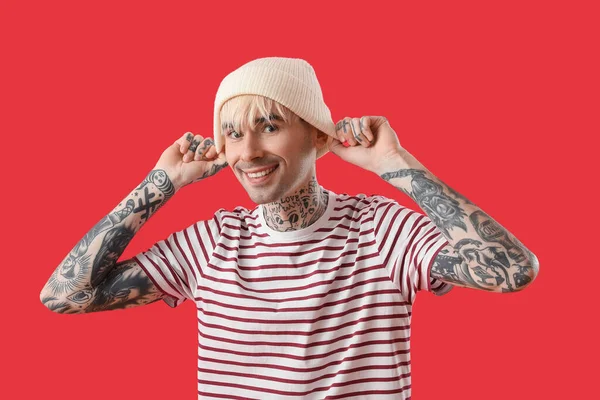 Tattooed young man in hat on red background