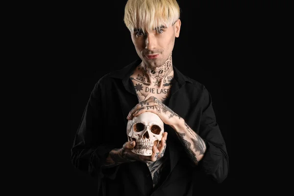 Tattooed young man with human skull on black background