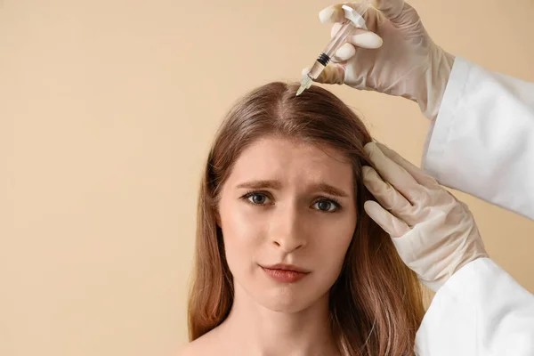 Young woman receiving injection for hair growth on beige background, closeup
