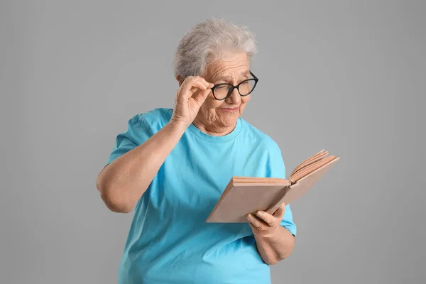 Mulher Sênior Óculos Lendo Livro Sobre Fundo Cinza — Fotografia de Stock