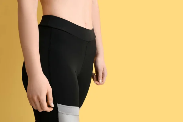 Sporty young woman in leggings on yellow background, closeup