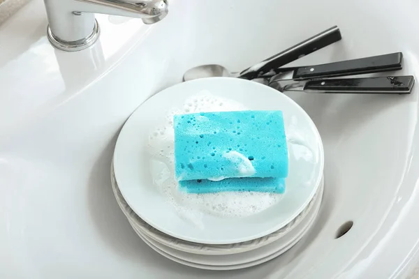 Plates with cleaning sponge and cutlery in sink, closeup