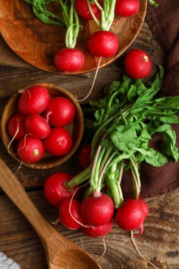 Tahta arka planda yaprakları olan bir tabak taze turp.