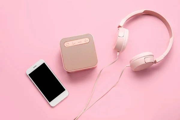 Mobile phone, headphones and speaker on pink background