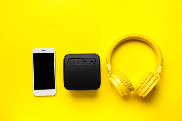Mobile phone, headphones and wireless speaker on yellow background