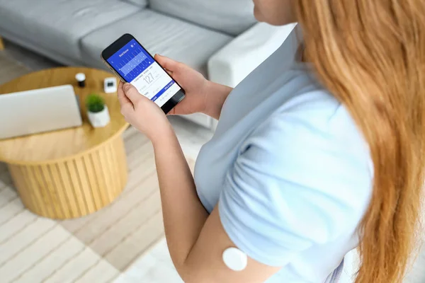携带葡萄糖传感器的妇女在家用手机测量血糖水平 — 图库照片