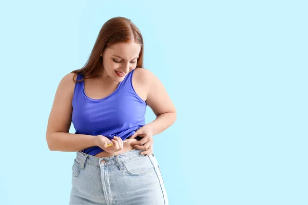 Woman with diabetes giving herself injection of insulin on light blue background