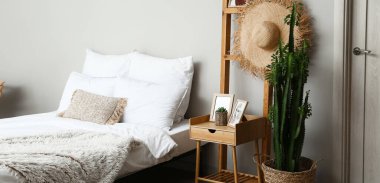 Yatak odasının içindeki büyük yatağın yanında yeşil kaktüs ve komodinin yanında.