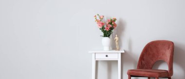 Bir buket çiçekli küçük masa, manken ve pembe sandalye, odanın ışık duvarının yanında. Tasarım için pankart