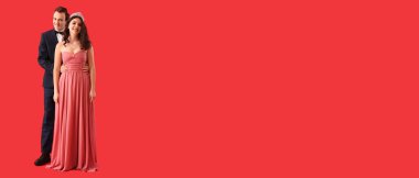 Mezuniyet balosu için kırmızı arka planda giyinen mutlu genç çift ve mesaj için yer var.