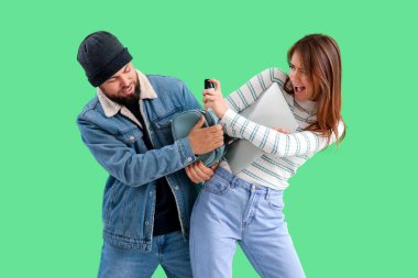 Young woman with pepper spray defending herself against thief on green background