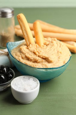 Lezzetli humus ve yeşil ahşap arka planda İtalyan Grissini tabağı.