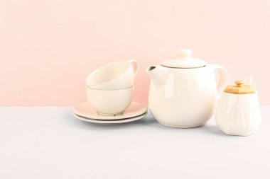 Çaydanlık, şeker kasesi ve fincanlar pembe arka planda.