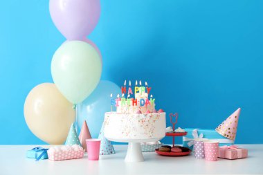 Mavi duvarın yanındaki masada farklı tatlılar olan doğum günü pastası.