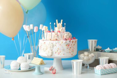 Mavi duvarın yanındaki masada farklı tatlılar olan doğum günü pastası.