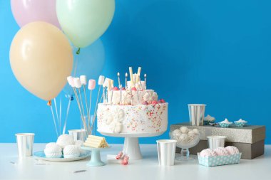 Mavi duvarın yanındaki masada farklı tatlılar olan doğum günü pastası.