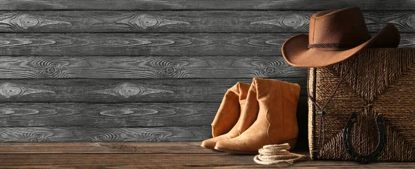 Cowboy hat with boots, box, horseshoe and lasso on dark wooden background with space for text