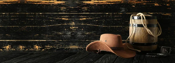 Cowboy hat with barrel, horseshoe and lasso on dark wooden background with space for text