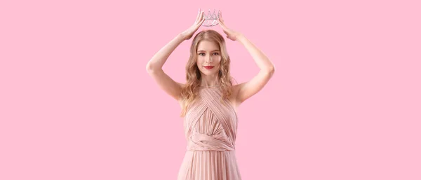 Beautiful young girl in prom dress and tiara on pink background