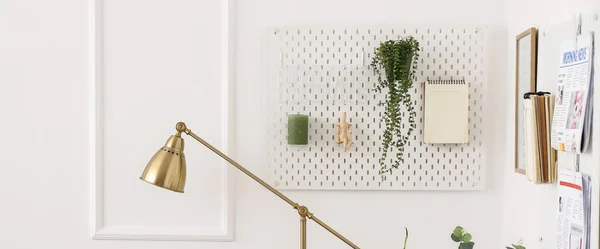 Hanging pegboard with houseplant, notebook and decor in interior of light room
