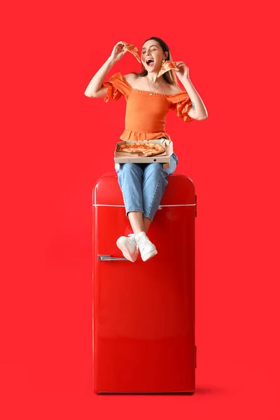 Piękna Kobieta Smaczną Pizzą Siedzi Lodówce Czerwonym Tle — Zdjęcie stockowe