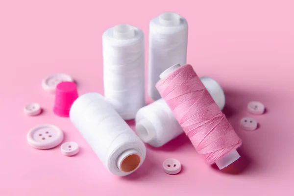 Sewing threads and buttons on pink background