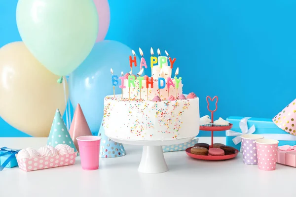 青い壁の近くのテーブルの上に異なるお菓子と誕生日ケーキ — ストック写真