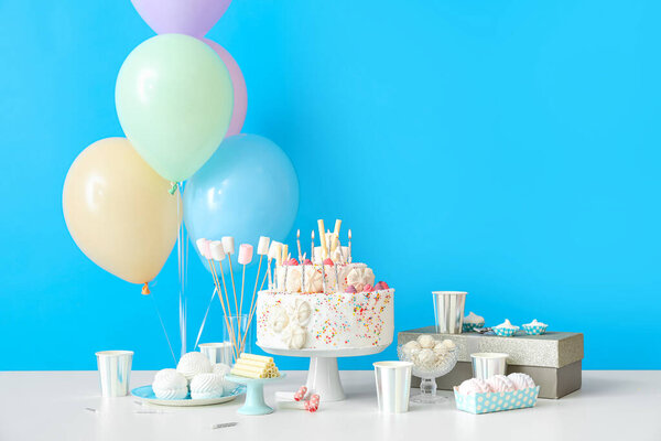 Торт на день рождения с различными сладостями на столе у голубой стены