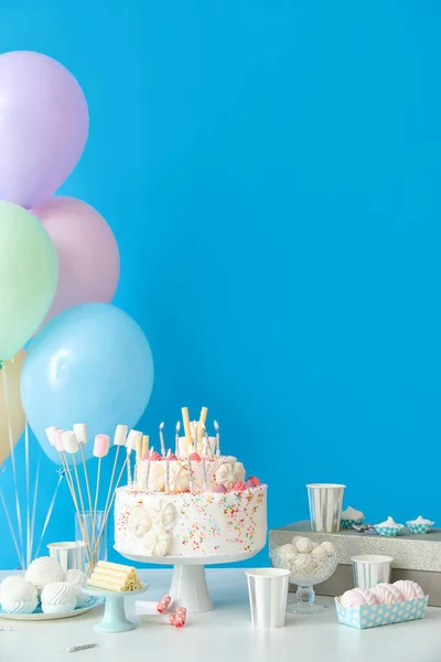 青い壁の近くのテーブルの上に異なるお菓子と誕生日ケーキ — ストック写真