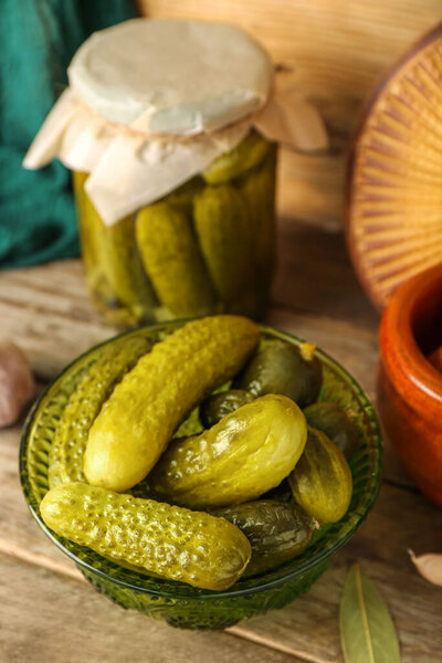 Jar and bowl with tasty canned cucumbers on wooden table