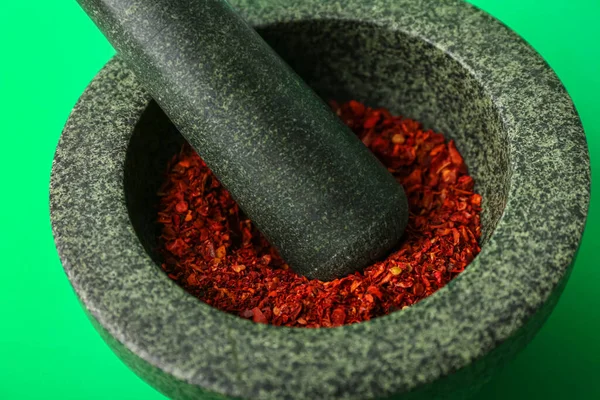 Mortar and pestle with spices on green background, closeup